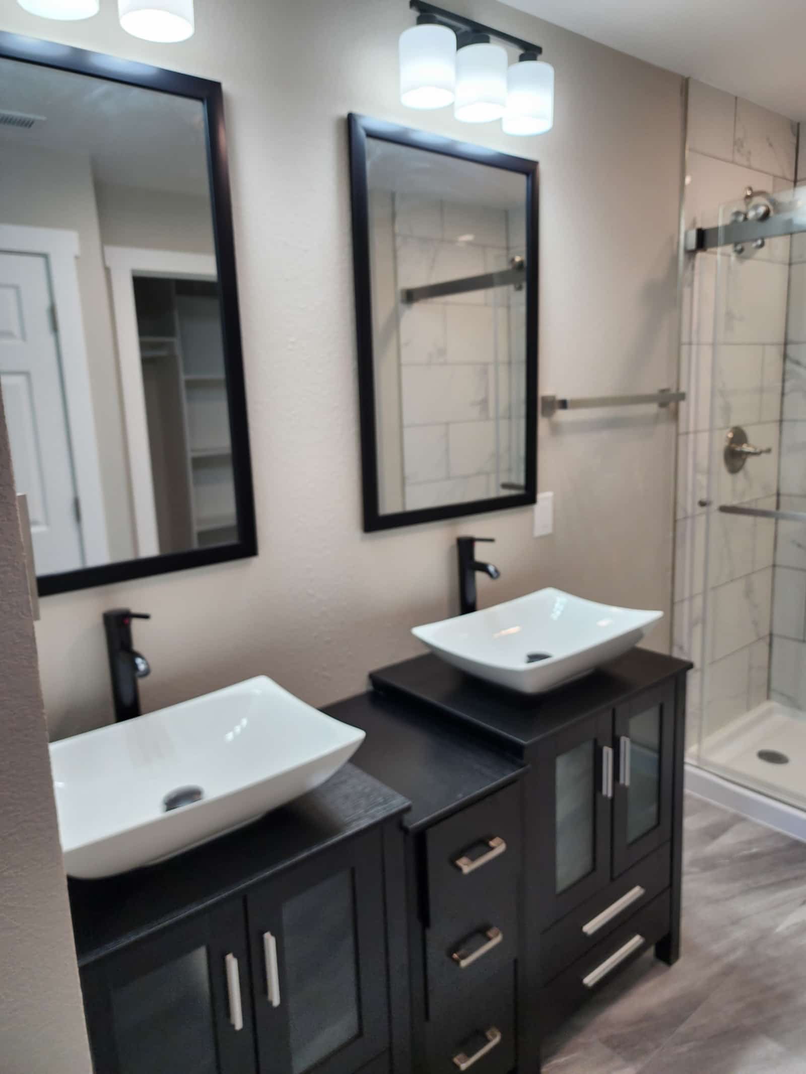 Finished bathroom with marble-look tile, twin vessel basins on a dark vanity and a glass walk-in shower