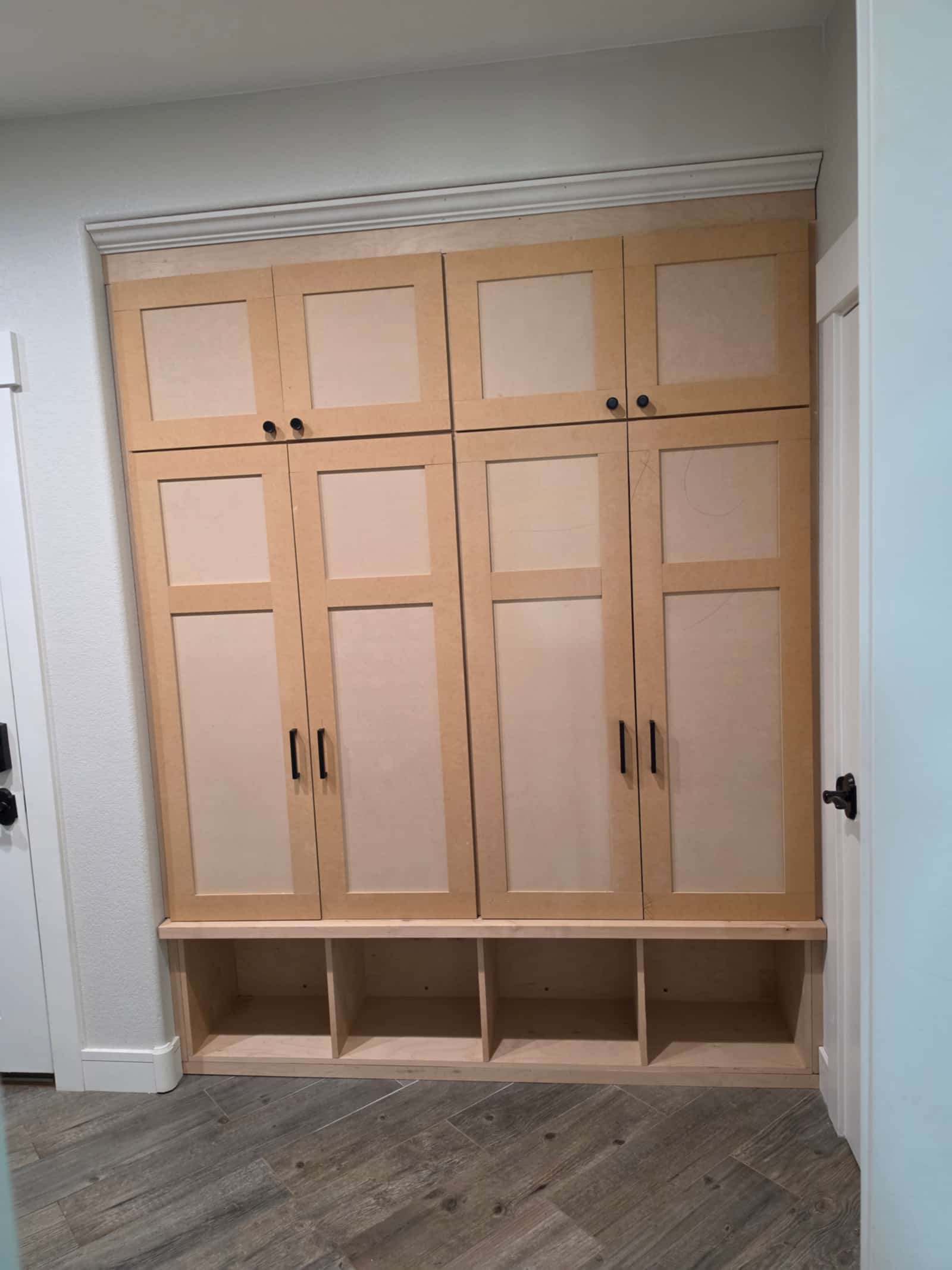 Floor-to-ceiling built-in cabinetry in pale timber with panelled doors and black handles