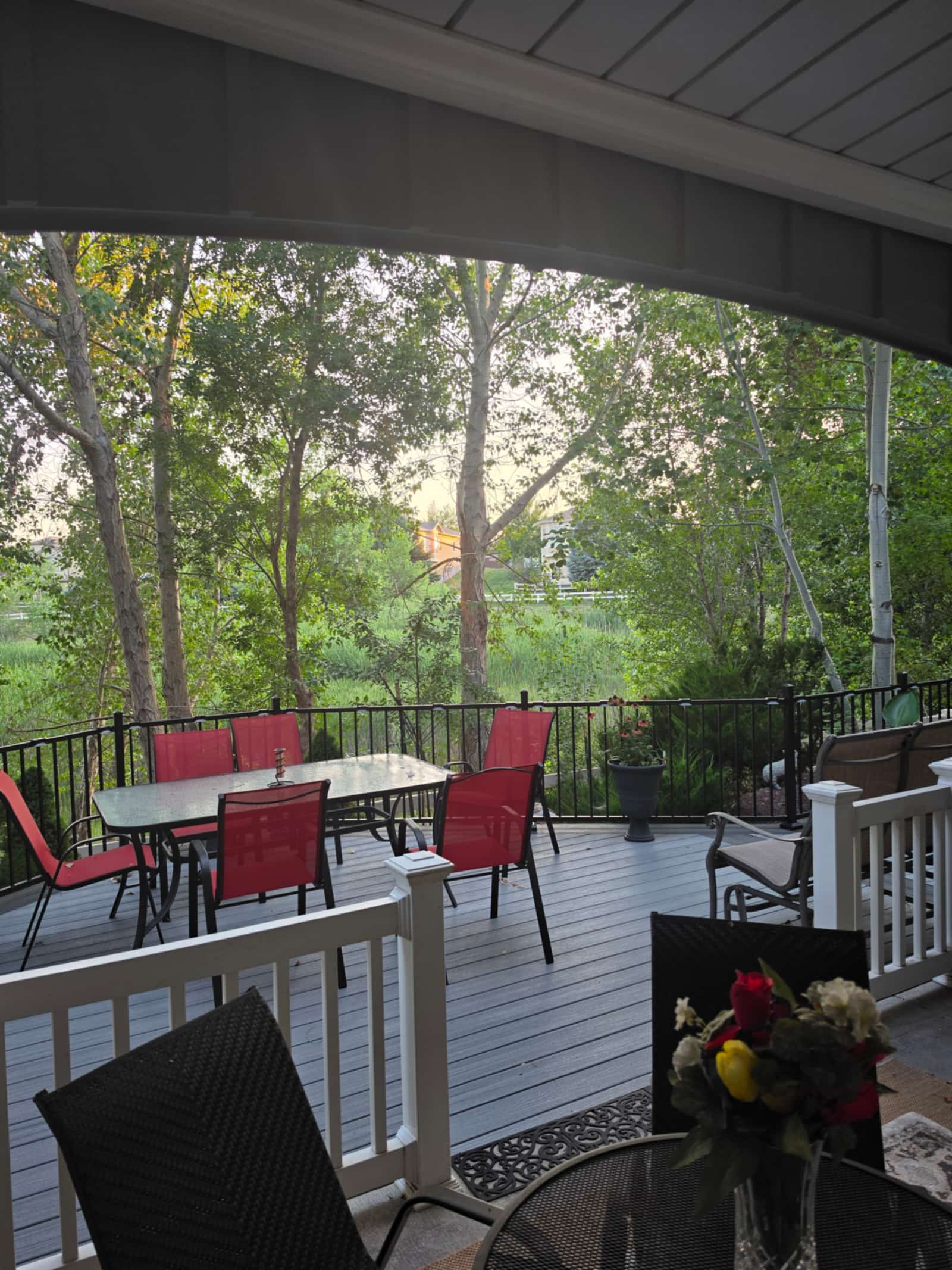 Furnished gray deck with red patio chairs and planters, mature trees behind