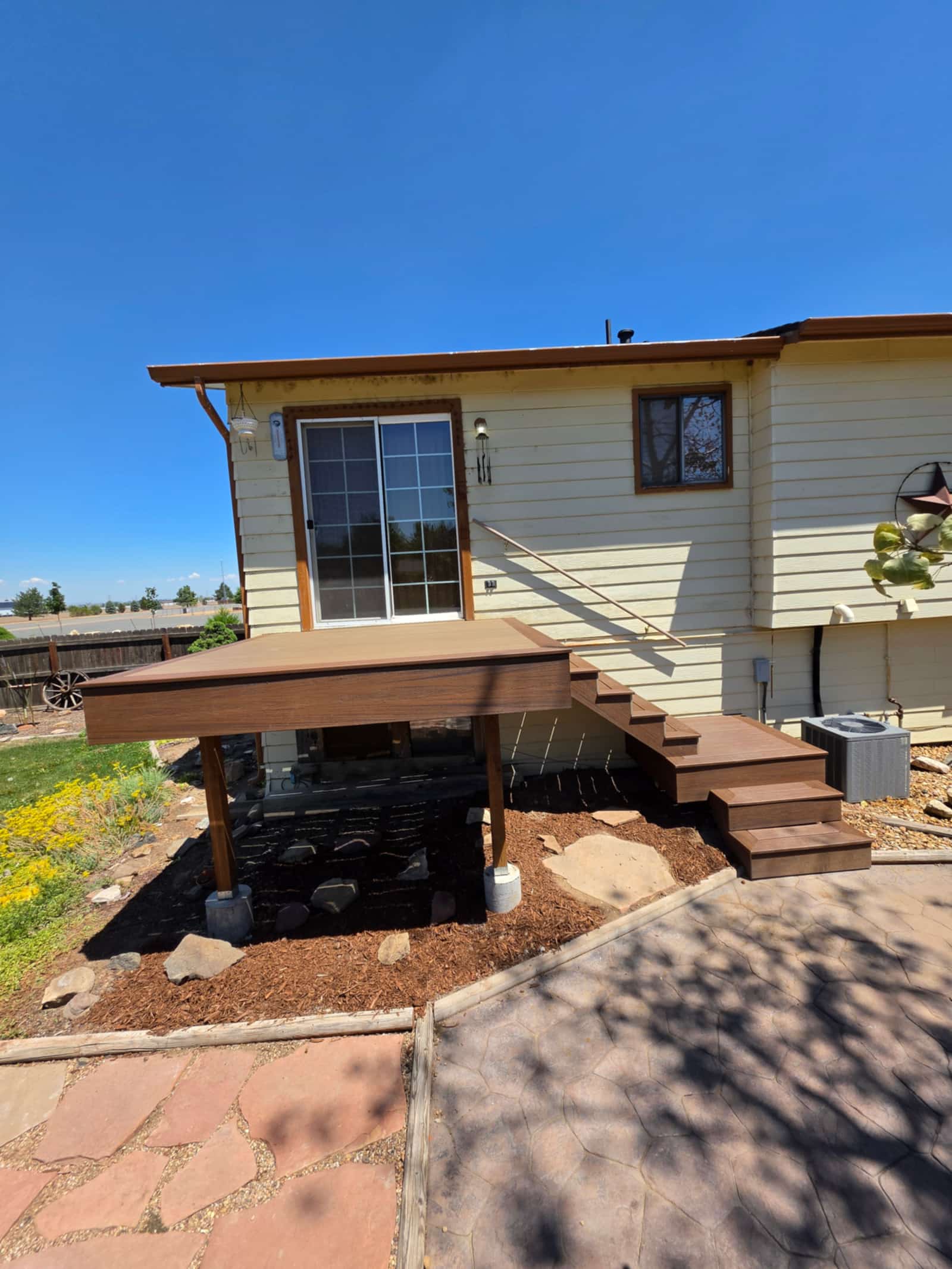 Newly built deck with wide steps down to a landscaped yard, cream siding behind