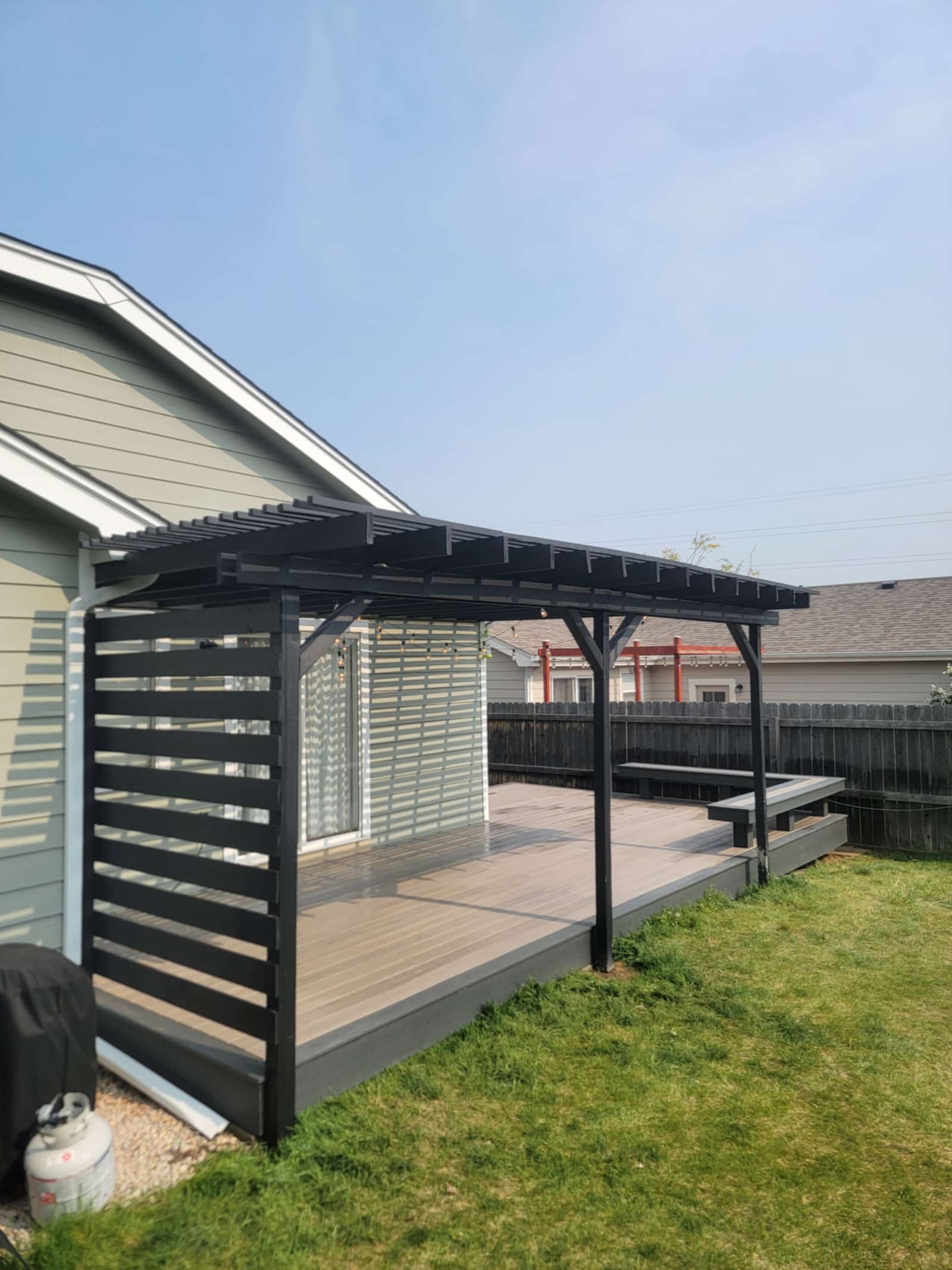 Black pergola over a composite deck with a built-in bench along the edge