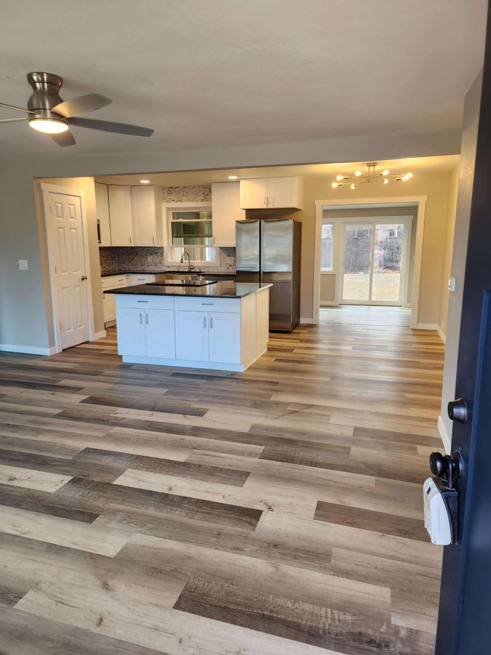 The same finished kitchen from the living room, showing the island, stainless fridge and pendant-lit dining area beyond