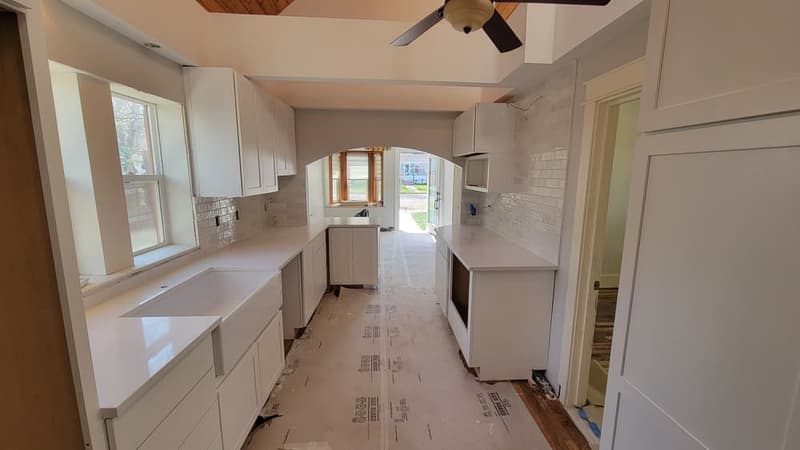 Kitchen part-way through installation: white shaker cabinets and pale worktops fitted, appliances not yet in and the floor still covered