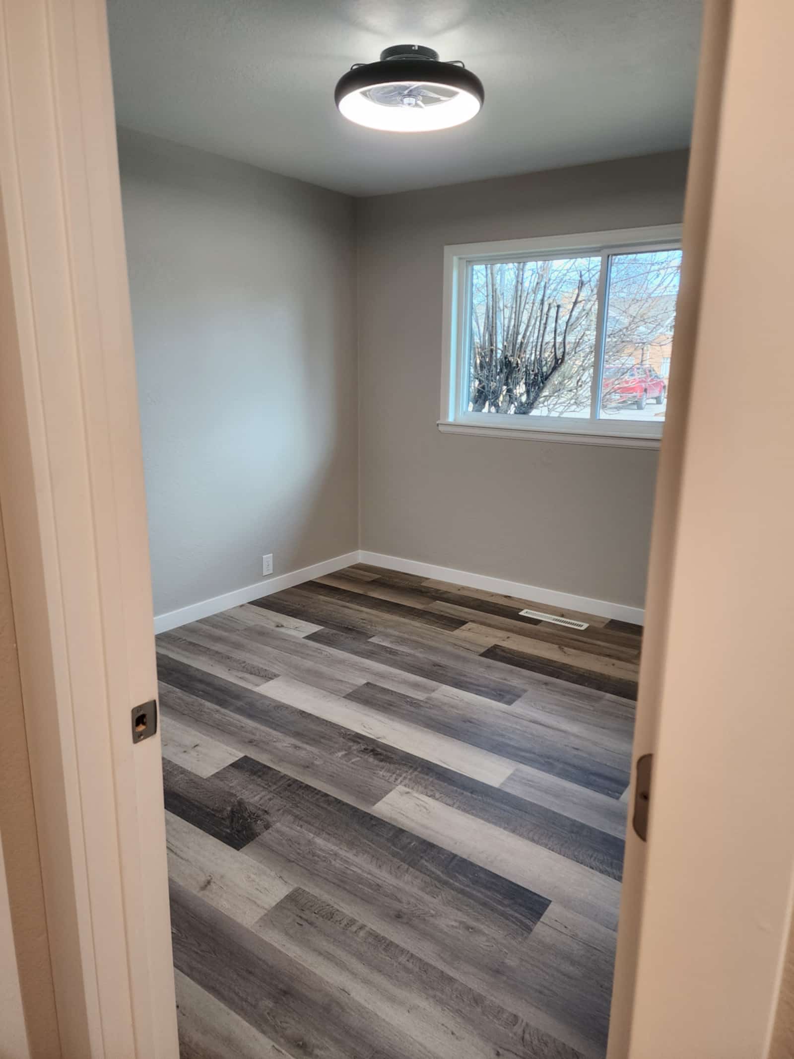 Finished bedroom with new flooring, a ceiling light and a window looking onto the street