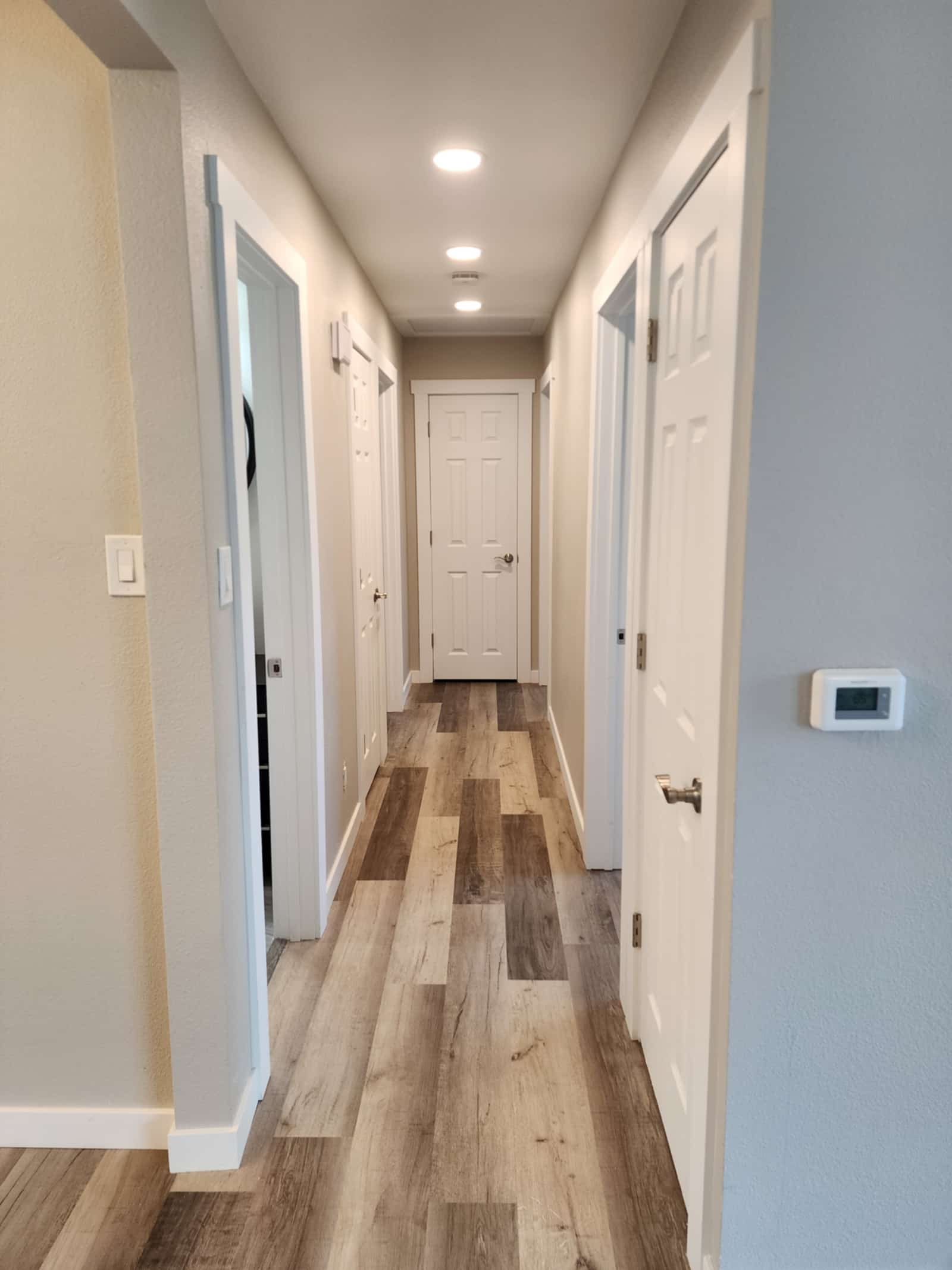Finished hallway with new doors, fresh trim, recessed lighting and plank flooring running through